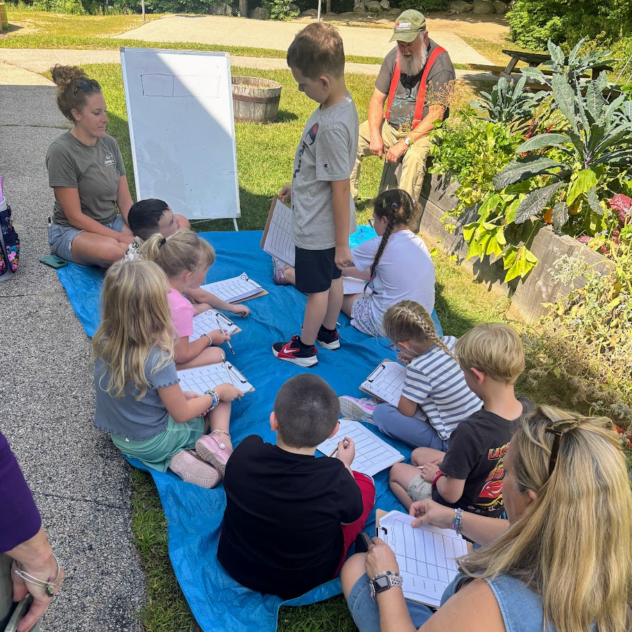 Students sit in a circle next to the school garden. 